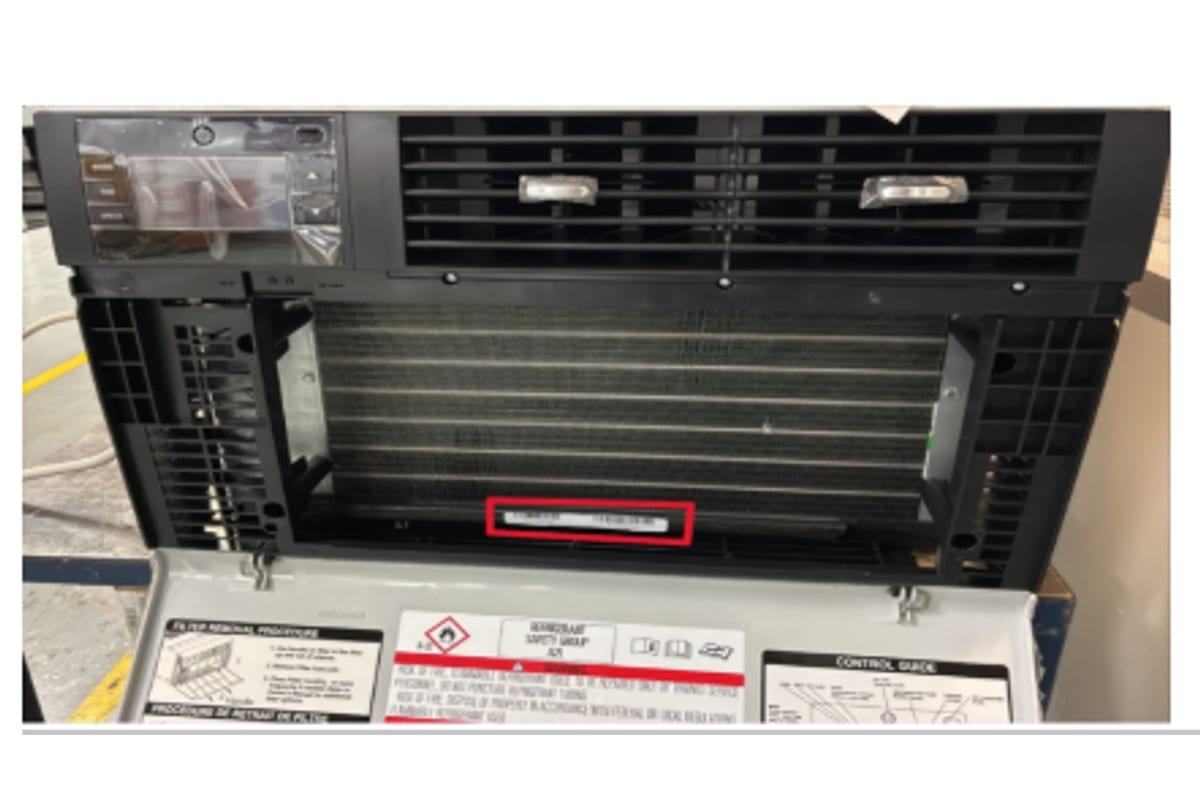 The open front panel of a window air conditioner showing the rating plate that carries the model and serial number